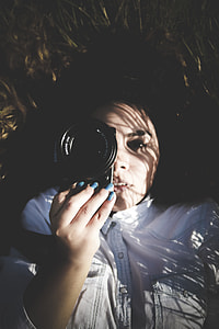 woman holding black camera while lying on grass field thumbnail