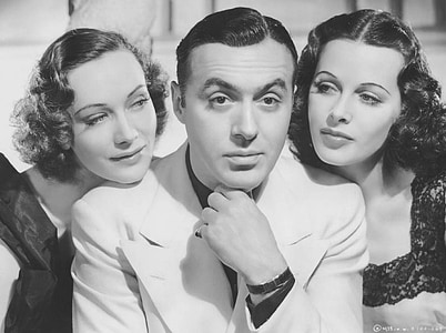 grayscale photo of man in suit jacket between two women thumbnail
