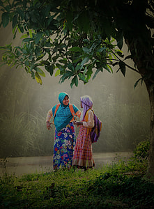 two women wearing standing beside green trees and river during daytime thumbnail