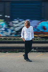 A fashionable man walks by train tracks with graffiti in the background thumbnail