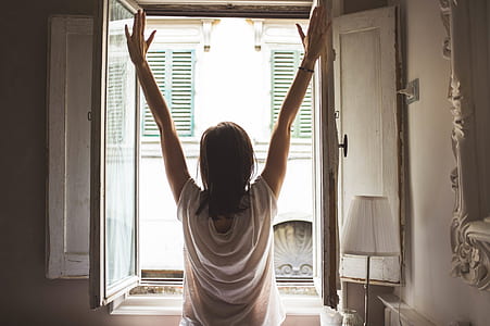 woman standing in front of opened window and putting her hands in the air thumbnail