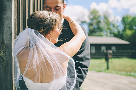 woman wearing white wedding dress with veil standing in front of man wearing black suit at daytime thumbnail