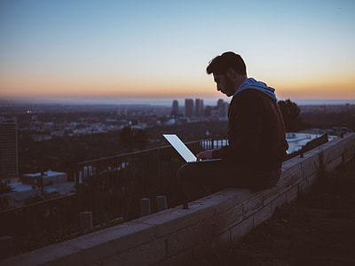man sitting on edge of building while using laptop computer thumbnail