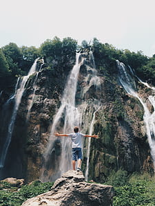 man standing on rock facing a waterfalls thumbnail