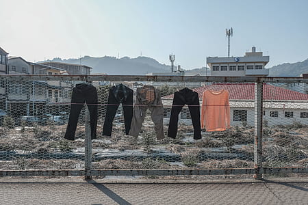 four assorted-color pants hanging on gray cyclone fence during daytime thumbnail