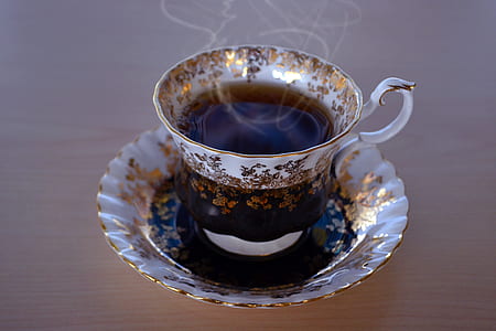 white and gold floral ceramic teacup filled with tea on top saucer thumbnail