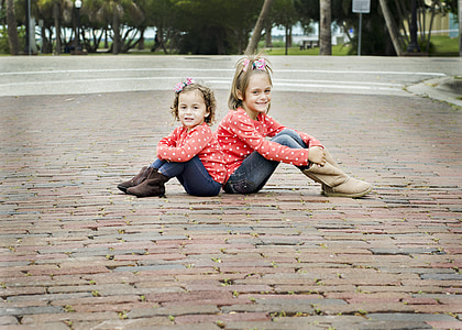 two girls in red polka dot sweater sitting on paver bricks thumbnail