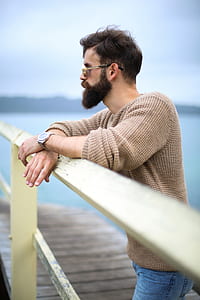man wearing brown sweater lean on white metal rail during daytime thumbnail