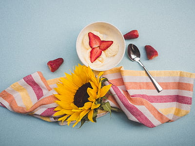 sliced strawberries in ceramic bowl beside spoon and sunflower thumbnail