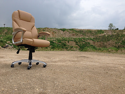 brown leather rolling armchair on brown dirt under cloudy sky thumbnail