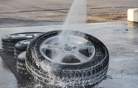 water spray pointing at gray 5-spoke vehicle wheel and tire set on gray concrete floor thumbnail