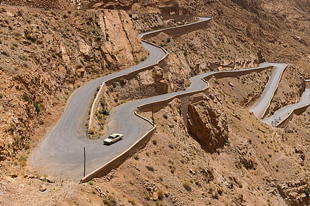 white car traveling on a narrow curve roads at daytime thumbnail