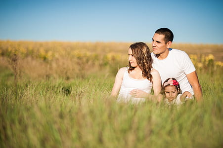 man, woman and child sitting on grass field during daytime thumbnail
