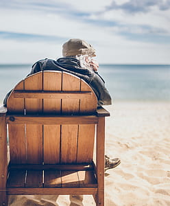 person sitting on brown wooden chair near body of water thumbnail