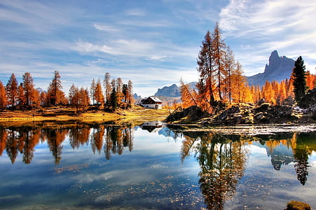 landscape photography of lake casting reflection of brown rocks, brown leaf trees, and white house thumbnail