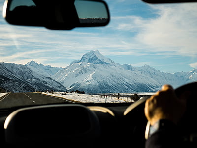 person driving car towards snow capped mountains at daytime thumbnail