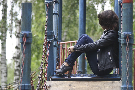 woman in black leather jacket sitting on metal surface on selective focus photo thumbnail