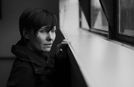 greyscale photo of woman wearing coat looking through the window thumbnail