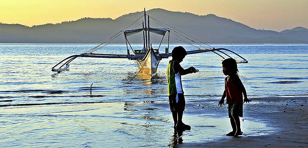 two children standing on shore near boat on ocean during daytime thumbnail