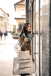 A young wearing almond brown overcoat and a turquoise blue scarf around her neck holding shopping bags in her hand thumbnail