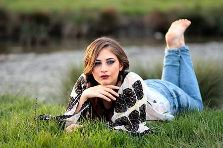 woman wearing black and white shirt and blue denim jeans reclining in grass thumbnail