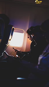 selective focus photography of person riding on plane while holding smartphone thumbnail