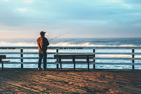 man wearing brown shirt and black pants holding fishing rod during daytime thumbnail