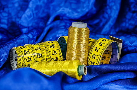 yellow tape measures and spools of thread on blue textile thumbnail