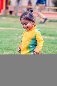 smiling girl wearing yellow and blue long-sleeved shirt on green grass thumbnail