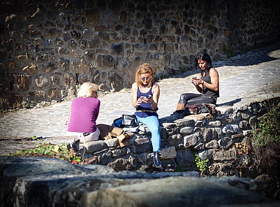 three women sitting on gray concrete pavement while using smartphones thumbnail