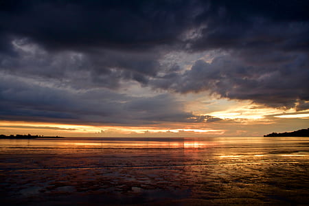 cloudy sky over calm body of water thumbnail
