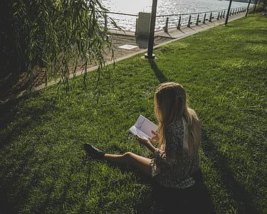 woman sitting while reading on grass field thumbnail