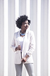 woman wearing white V-neck shirt with white coat standing beside white wall during daytime thumbnail