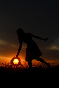 silhouette of woman holding wreath with sun in background during golden hour thumbnail