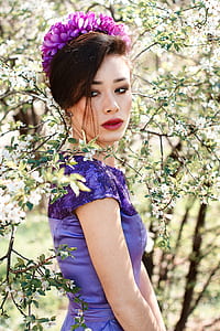 woman posing near green leaf plant with purple flower headdress and purple dress thumbnail
