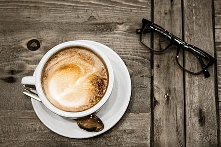 black framed Wayfarer-style eyeglasses beside white ceramic teacup filled with coffee thumbnail
