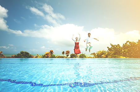 man and woman jumping on pool during daytime thumbnail