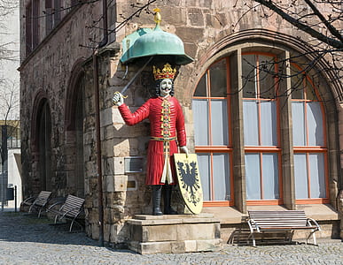 man standing holding sword and shield statue beside house thumbnail