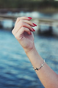 person with red manicure and silver-colored sideway cross bracelet thumbnail