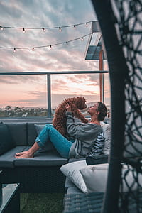 woman in blue denim pants holding brown dog on couch thumbnail