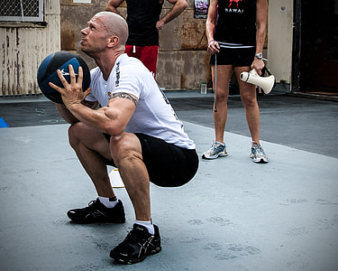 man squatting and holding black medicine ball thumbnail
