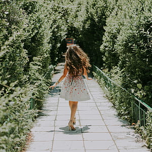 Photography of Woman in White and Red Floral Midi Dress Walking on Pathway thumbnail