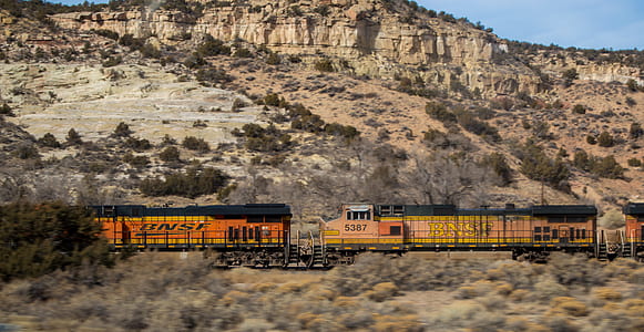 orange and black train travelling between desert thumbnail