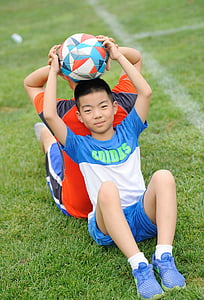 boy lifting soccer ball on grass field thumbnail