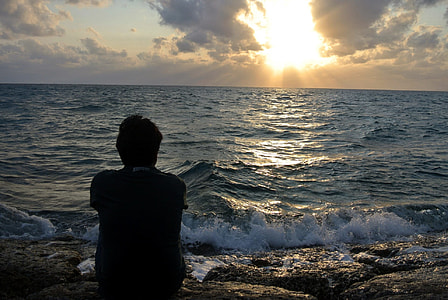 silhouette of man sitting on seashore during golden hour thumbnail