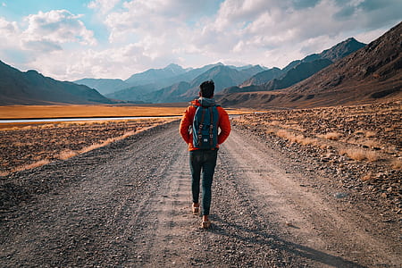 person wearing orange hoodie while waking on gray road thumbnail