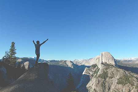 man raising hands while standing on hill during daytime thumbnail