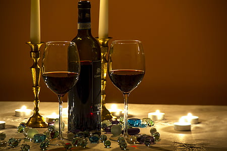 two filled wine glasses on top of white surface near wine bottle and marble toys thumbnail