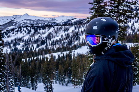 man looking sideways wearing black helmet in front of snow mountain thumbnail