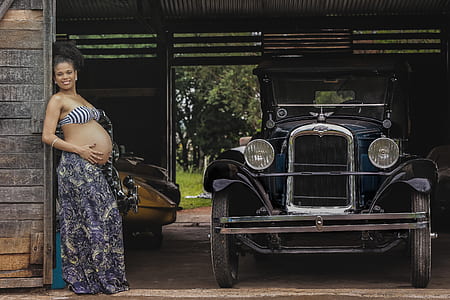 pregnant woman standing next to classic black car thumbnail